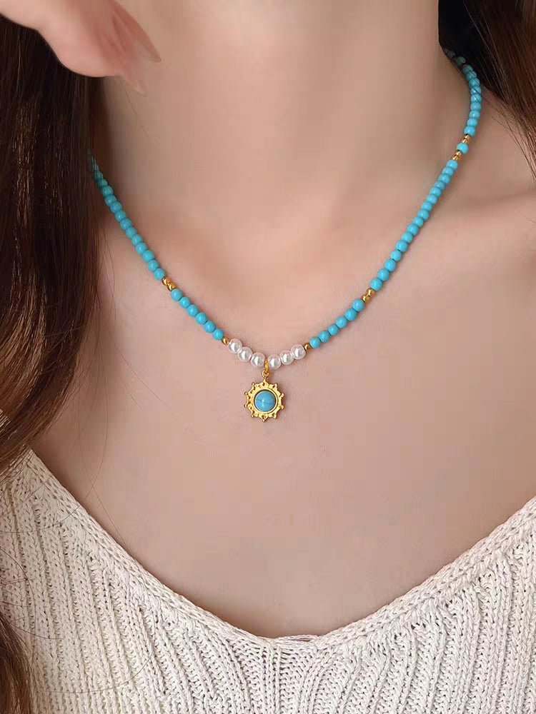 Model wearing turquoise bead necklace with gold sunburst pendant paired with white knit sweater