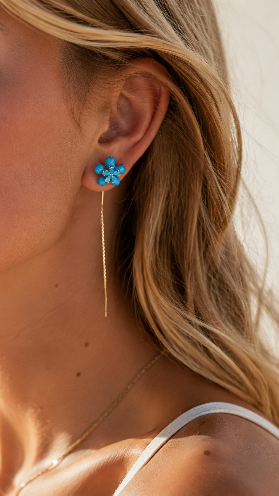 Blonde model with sun-kissed skin wearing turquoise flower gold threader chain earrings in golden hour light