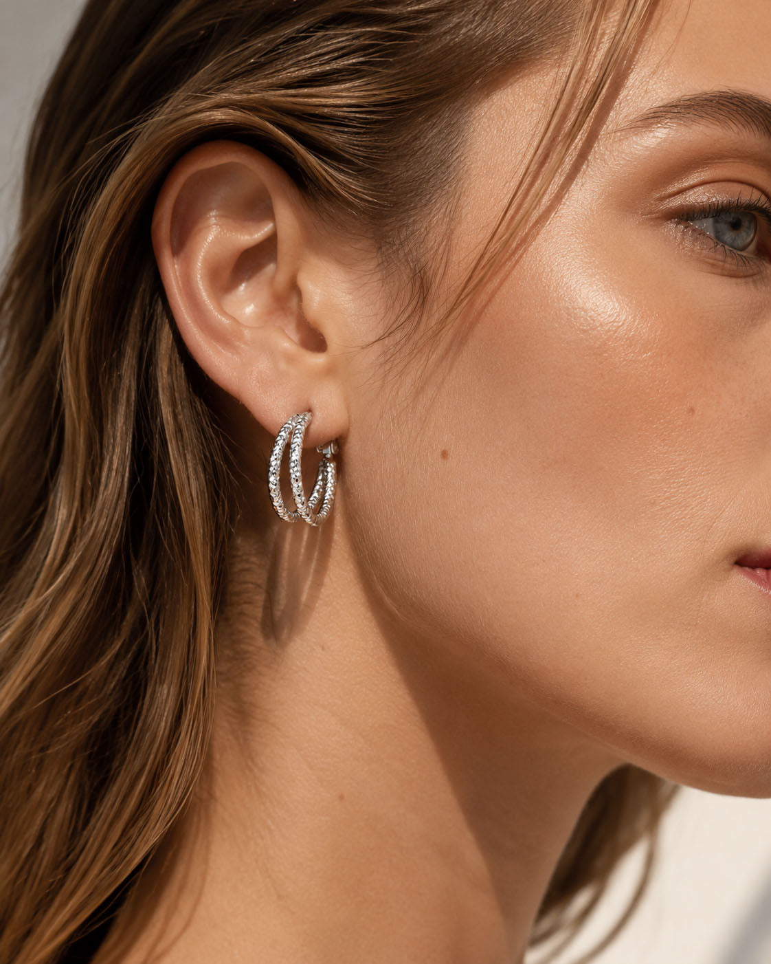 Elegant woman wearing vintage textured double hoop earrings in white gold-tone.