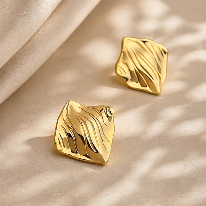 Elegant 18K gold-tone textured geometric earrings resting gracefully on an aesthetic stone surface with soft silk and beautiful shadow play.