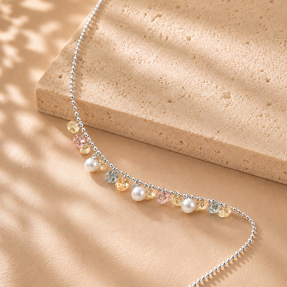 Close up of pastel zirconia and pearl drops on a delicate white gold-tone chain resting on a textured stone surface.