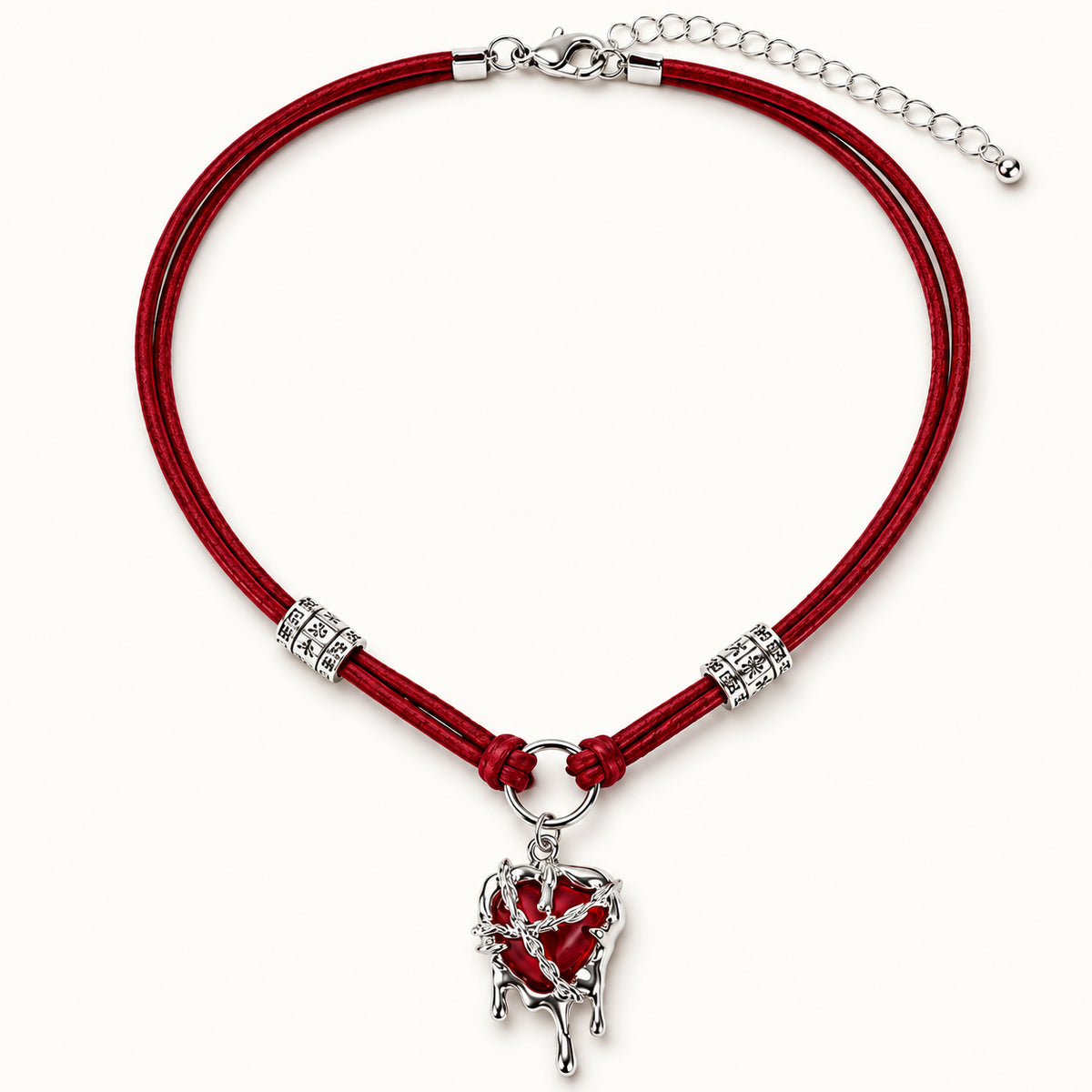 Flatlay view of burgundy suede choker with silver molten liquid dripping heart pendant on beige background