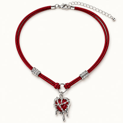 Flatlay view of burgundy suede choker with silver molten liquid dripping heart pendant on beige background