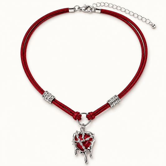 Flatlay view of burgundy suede choker with silver molten liquid dripping heart pendant on beige background