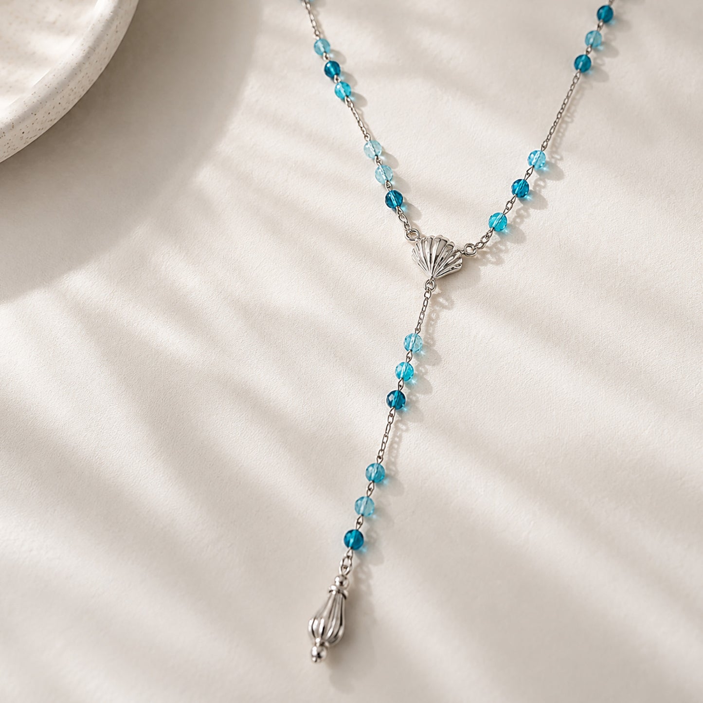 Coastal-inspired long drop necklace featuring blue gemstones and a teardrop finish displayed on a textured plaster tray.