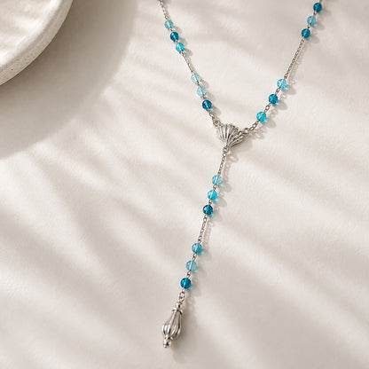 Coastal-inspired long drop necklace featuring blue gemstones and a teardrop finish displayed on a textured plaster tray.