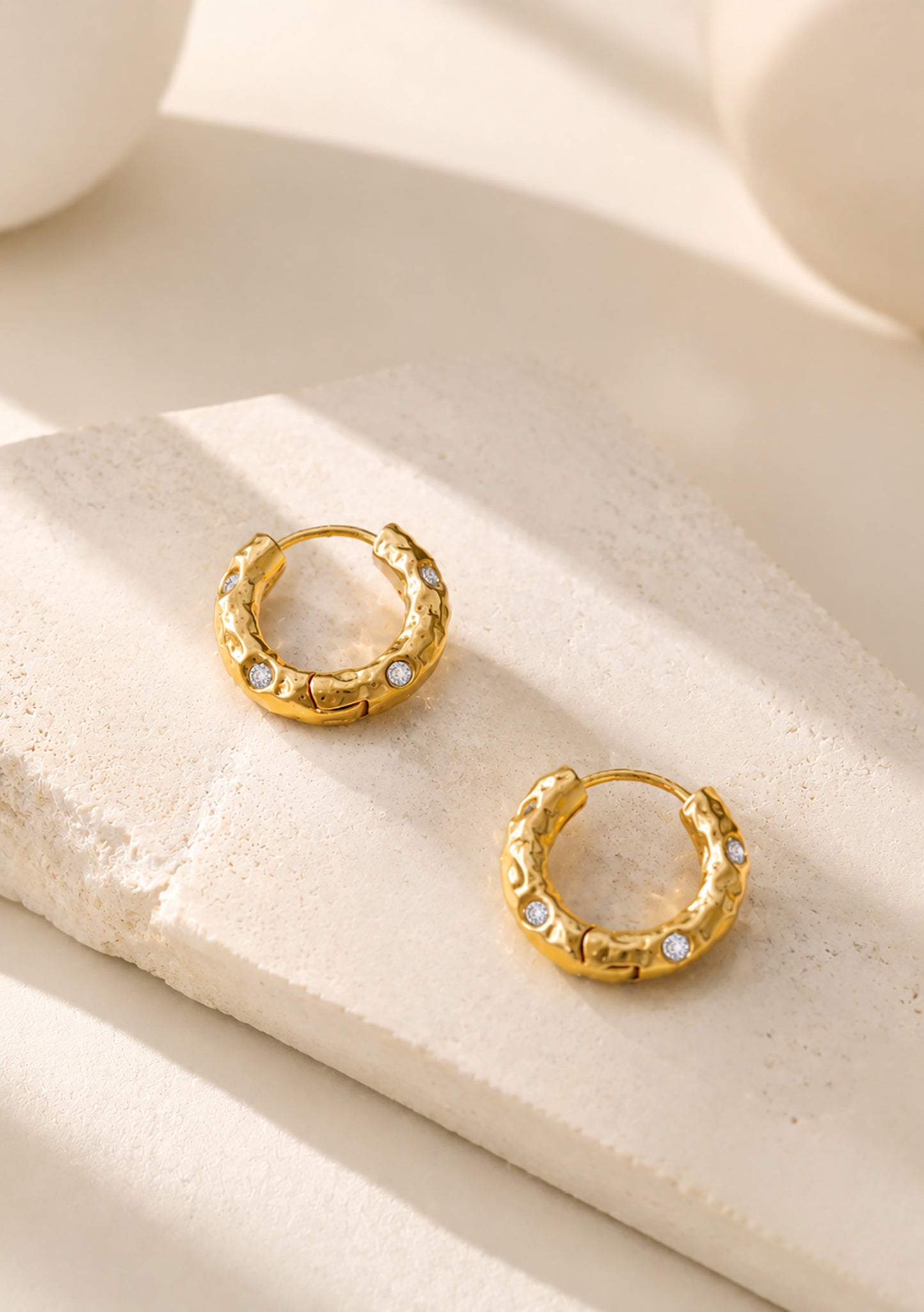 Pair of vintage-inspired hammered gold-tone hoop earrings resting beautifully on a textured aesthetic stone block.