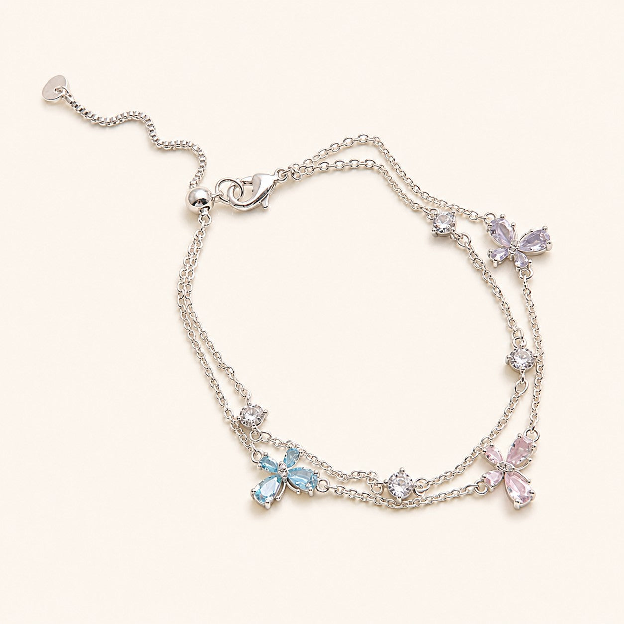 Double layer silver chain bracelet with pastel pink blue lavender four-leaf flower charms and slider toggle on cream background