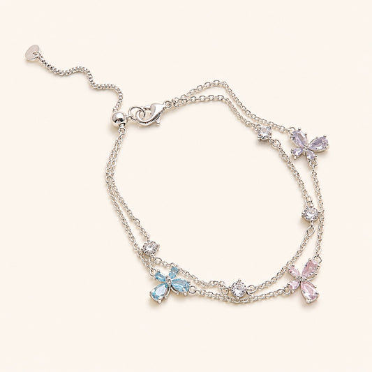Double layer silver chain bracelet with pastel pink blue lavender four-leaf flower charms and slider toggle on cream background