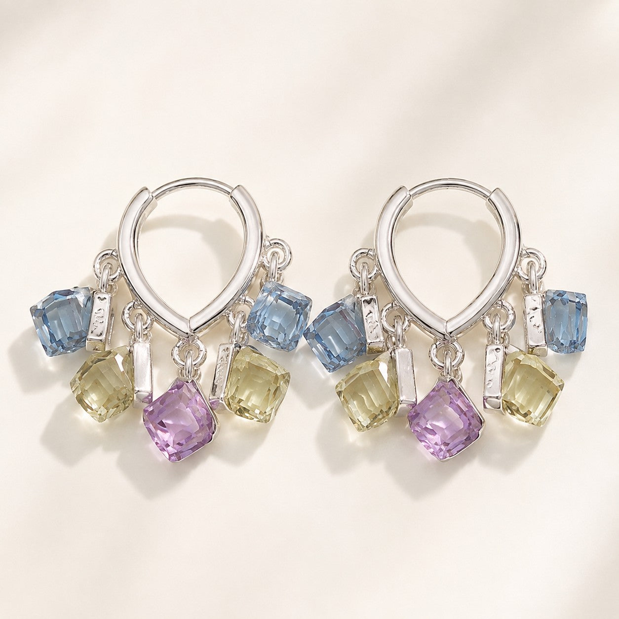 Pair of silver finished huggie hoop earrings featuring dangling pastel blue, yellow, and purple sugar cube crystals