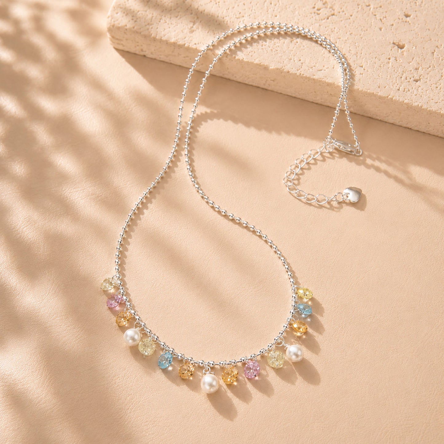 Beautiful rainbow colored zirconia and pearl fringe necklace displayed with soft shadows on a beige background.