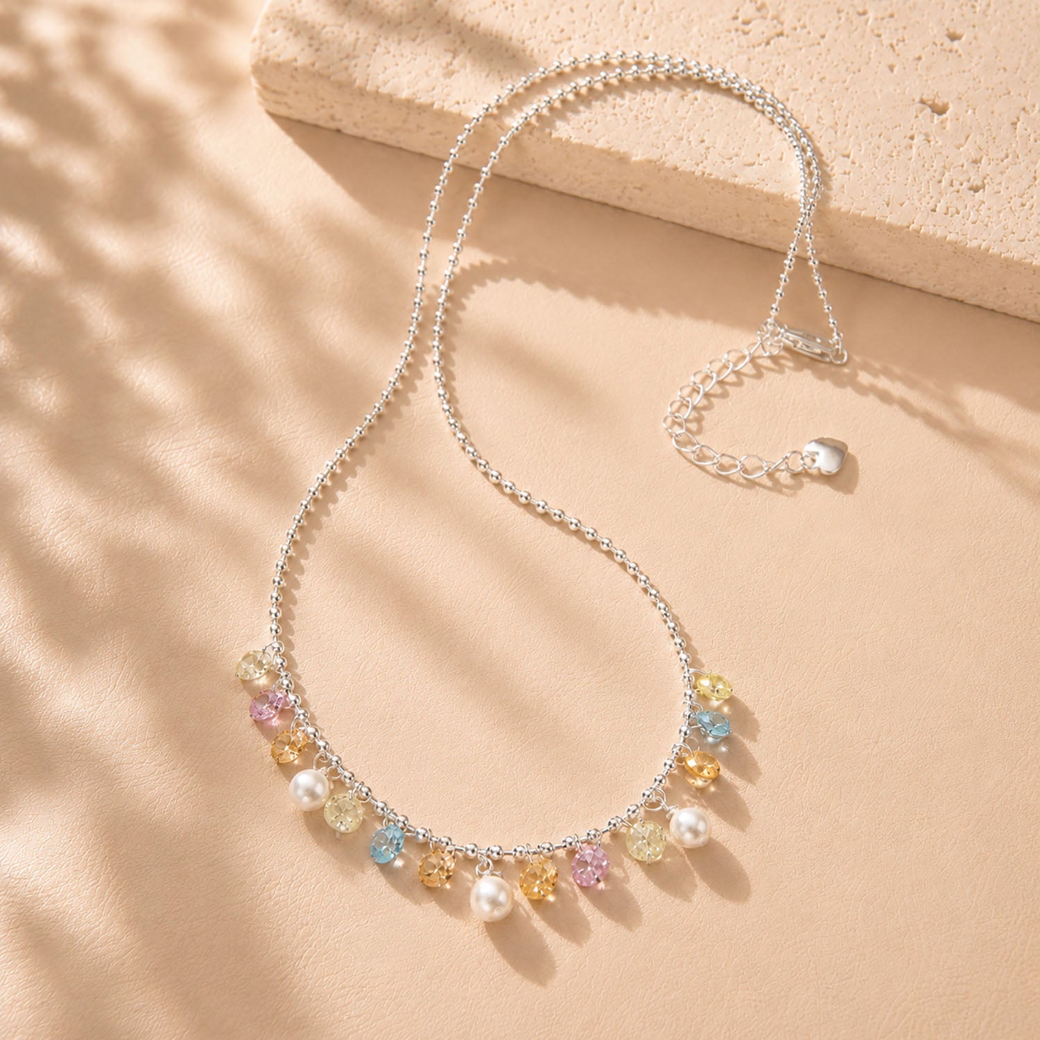 Beautiful rainbow colored zirconia and pearl fringe necklace displayed with soft shadows on a beige background.