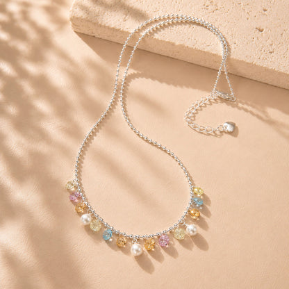 Beautiful rainbow colored zirconia and pearl fringe necklace displayed with soft shadows on a beige background.