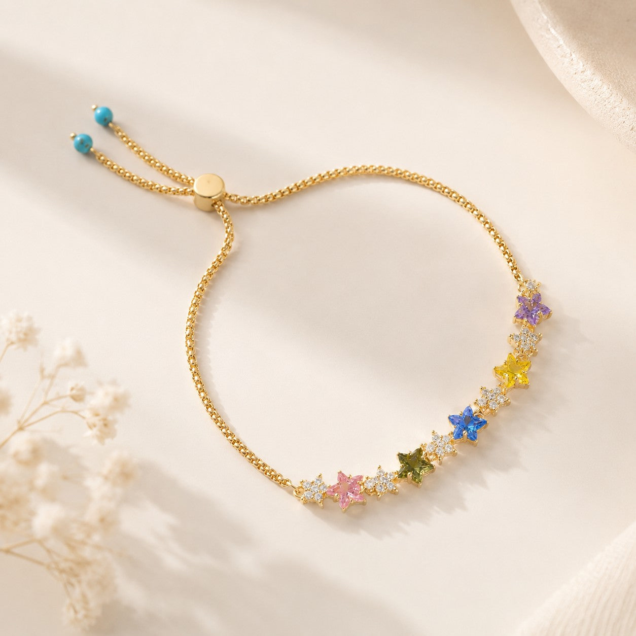 18K gold plated rainbow star cubic zirconia adjustable bolo slider bracelet with turquoise accent beads on beige surface