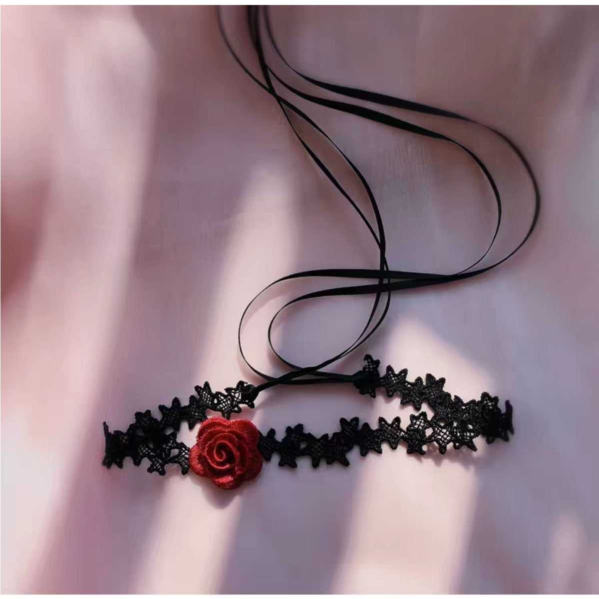 Close-up of gothic black bat lace choker with crimson rose on soft silk background