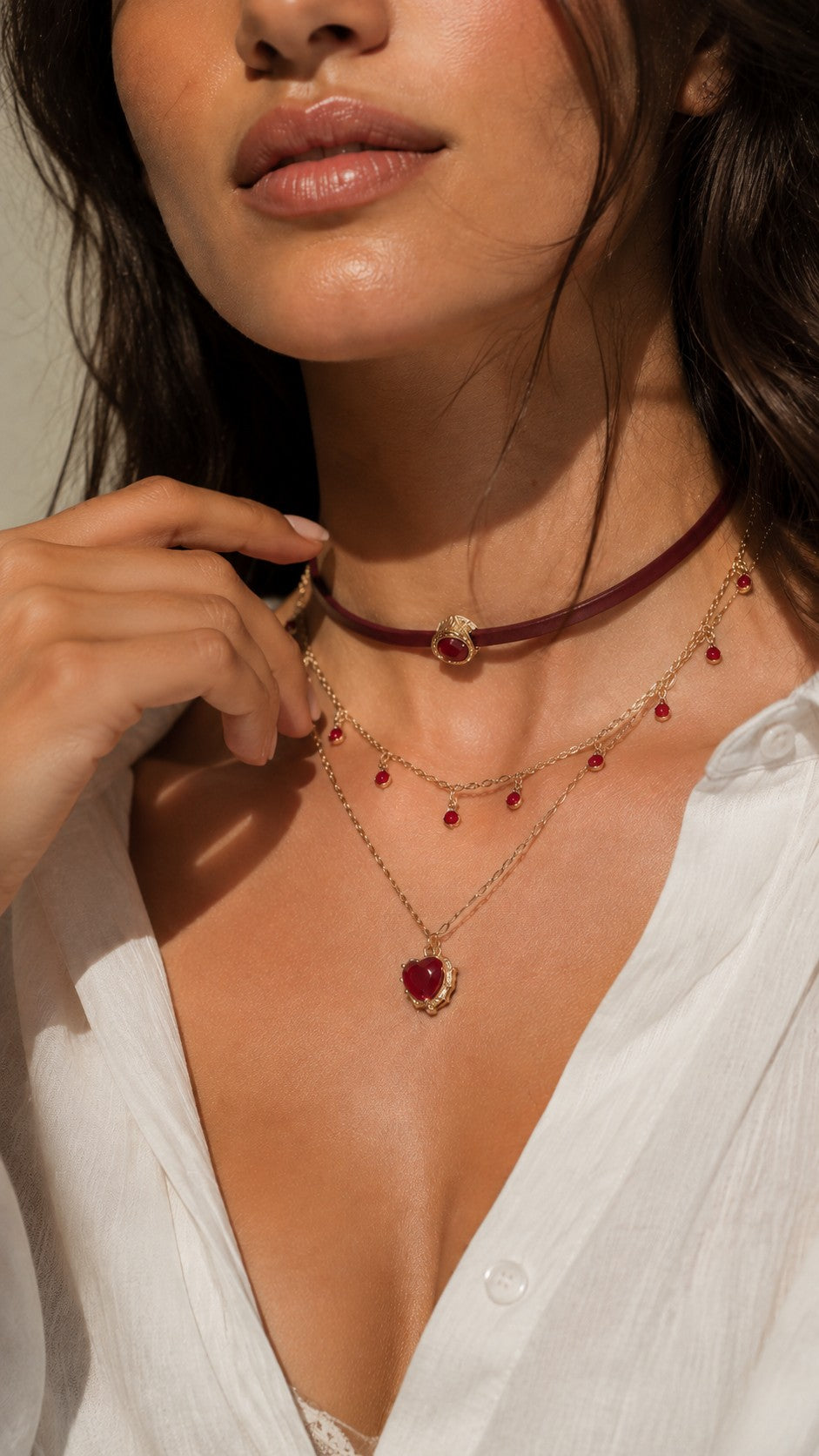 Model hand touching neck showcasing dark romantic burgundy leather layered heart necklace with white shirt
