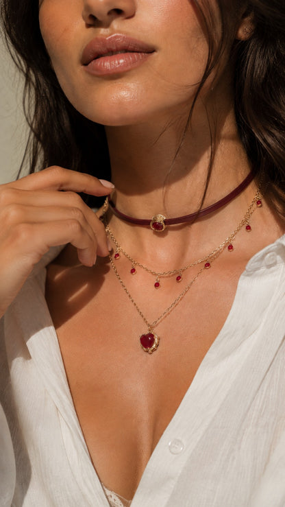 Model hand touching neck showcasing dark romantic burgundy leather layered heart necklace with white shirt