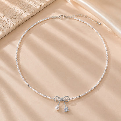 Romantic pearl necklace with a white gold-tone ribbon bow resting on textured stone and soft silk.