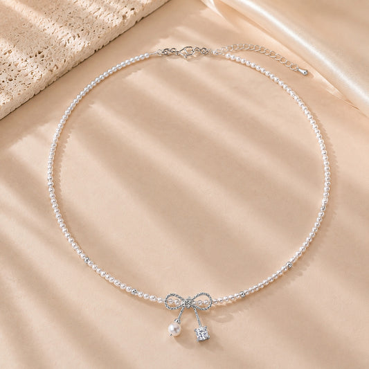 Romantic pearl necklace with a white gold-tone ribbon bow resting on textured stone and soft silk.