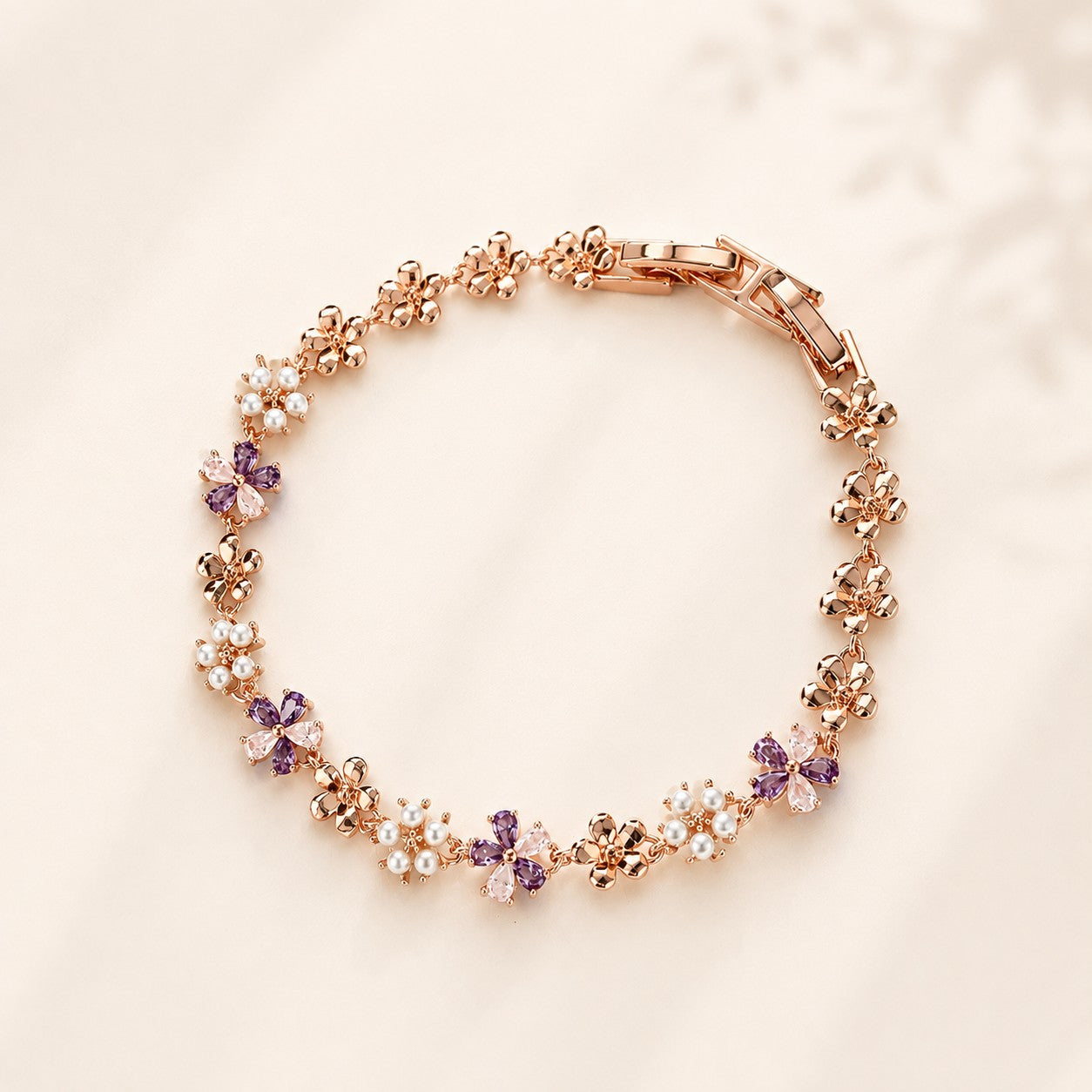 Flatlay view of a rose gold wisteria flower bracelet with lavender CZ crystals and pearls
