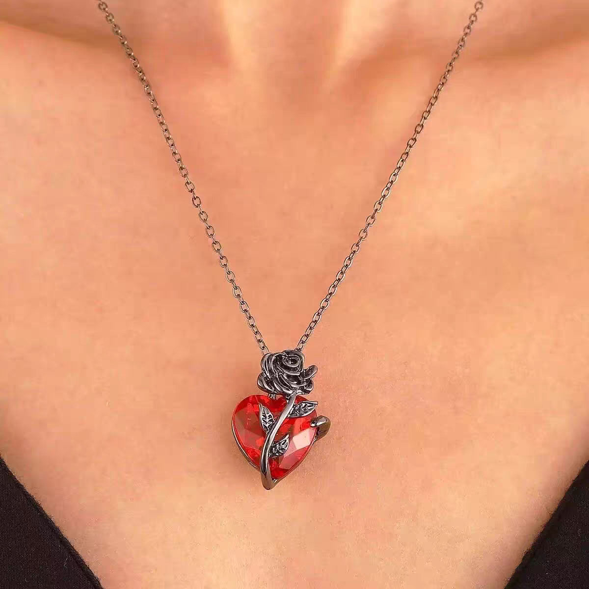 Close-up of model wearing black metal rose red crystal heart necklace on collarbone