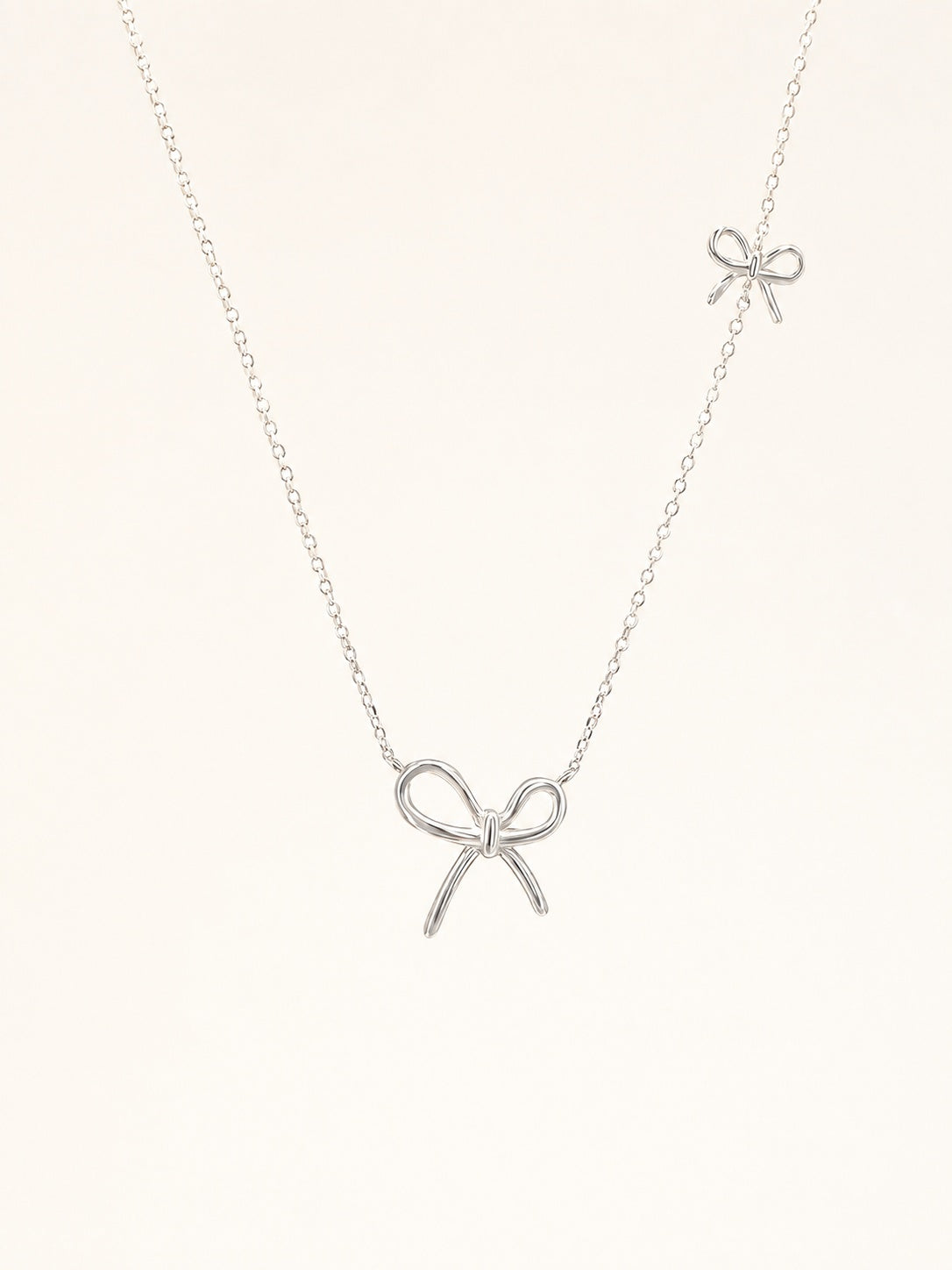 Flat-lay view of a delicate S925 sterling silver chain necklace featuring two asymmetric wire bow pendants.