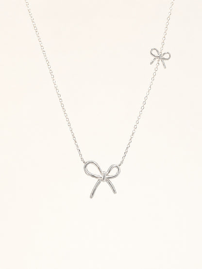 Flat-lay view of a delicate S925 sterling silver chain necklace featuring two asymmetric wire bow pendants.
