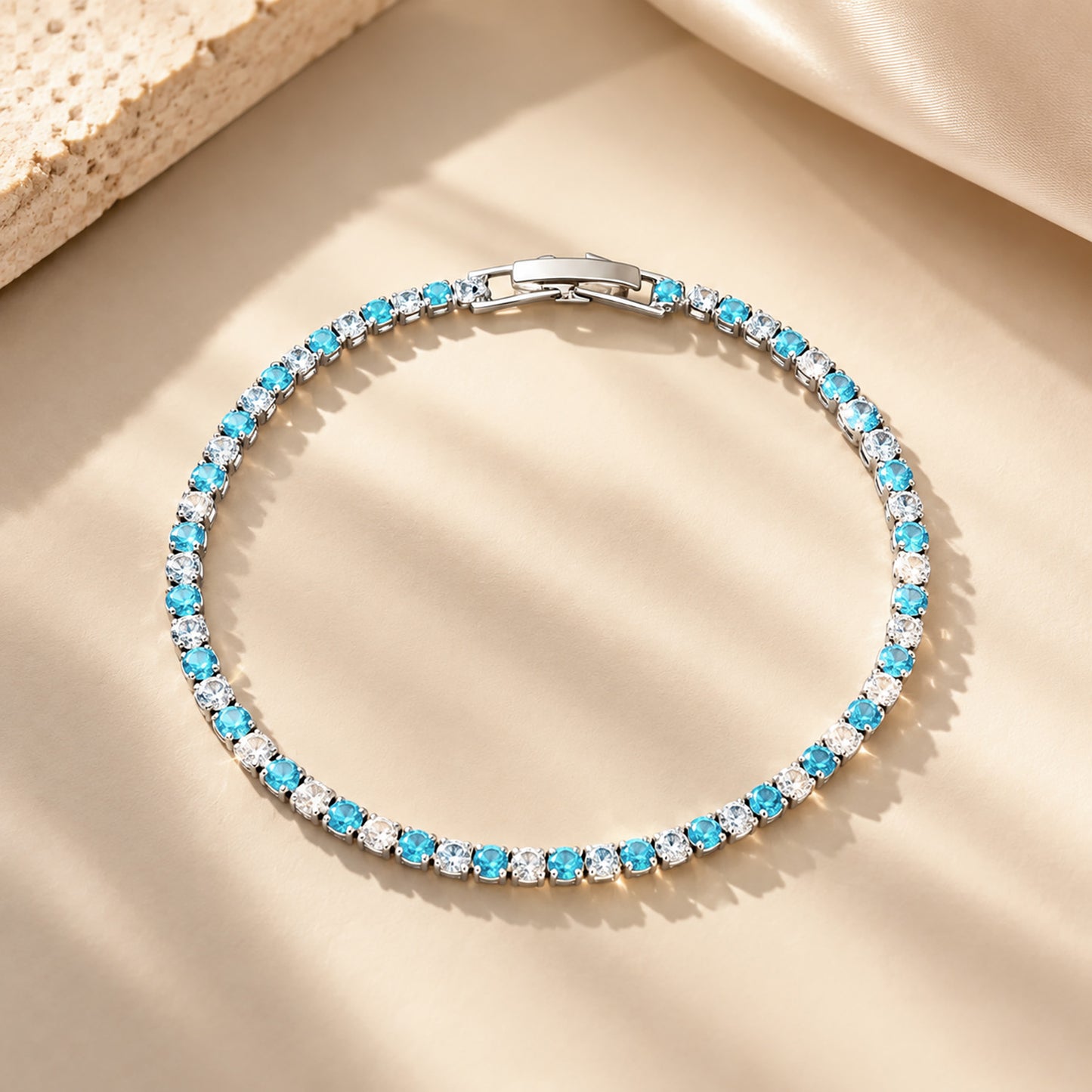 Elegant sapphire blue and clear zirconia tennis bracelet resting on a minimalist geometric plaster and silk background.