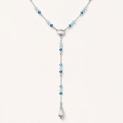 Minimalist flat lay of an elegant Y-necklace featuring a central seashell, blue gemstones, and a teardrop pendant on a white background.