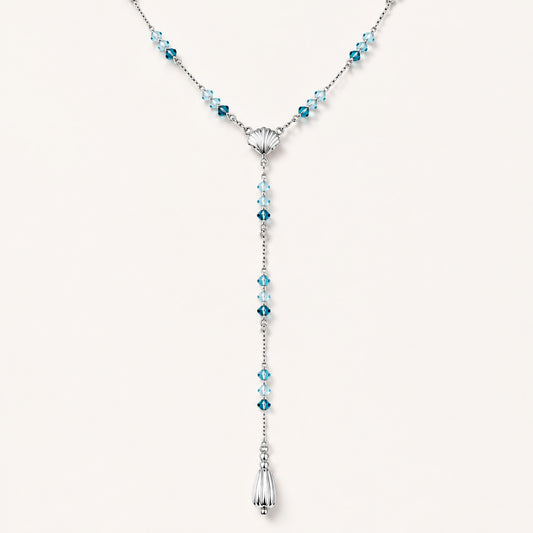Minimalist flat lay of an elegant Y-necklace featuring a central seashell, blue gemstones, and a teardrop pendant on a white background.