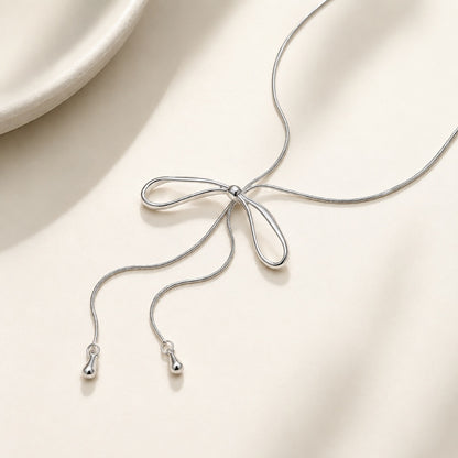 Elegant silver-plated bow tie lariat necklace resting gracefully on an aesthetic stone tray and soft silk fabric.