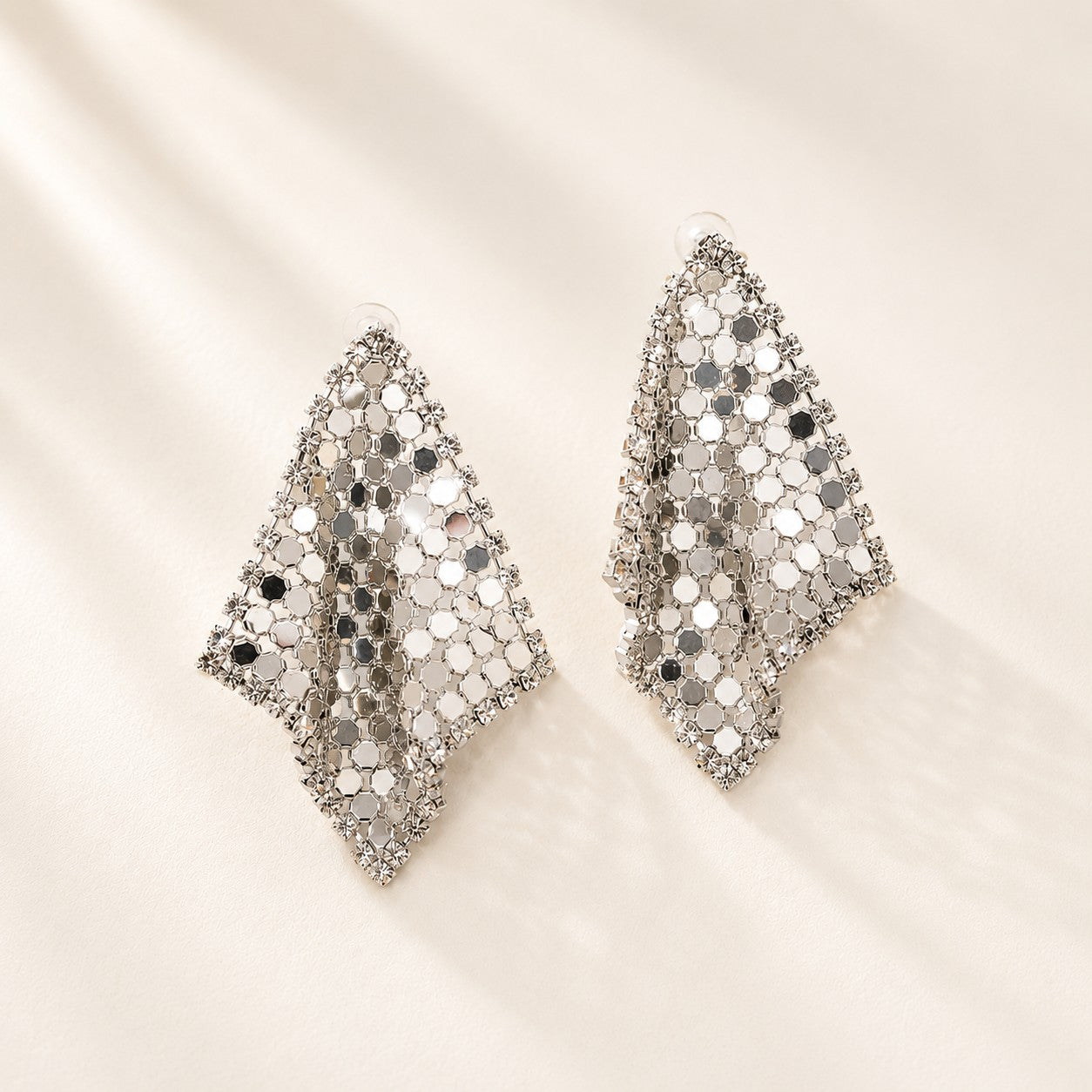 Flatlay view of pair of silver liquid metal mesh scarf rhombus stud earrings with clear CZ crystals