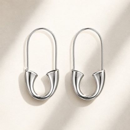 Pair of high-shine silver safety pin U-shape drop earrings on neutral beige background