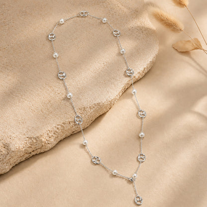 Elegant silver-tone Y-necklace featuring mother-of-pearl and anchor links, resting on a textured stone surface with dried botanicals.