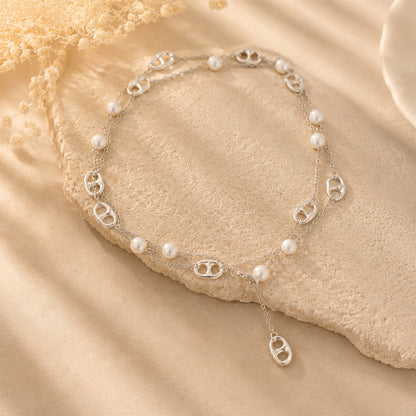 Silver-tone pearl and anchor chain Y-necklace draped elegantly over a textured stone surface.