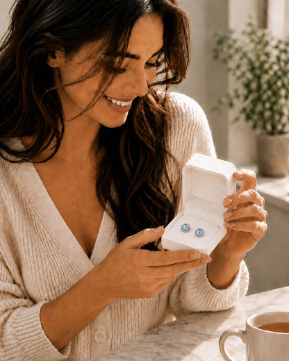 Smiling woman looking at a beautiful pair of sapphire blue halo zirconia stud earrings inside a white Moonlook gift box.