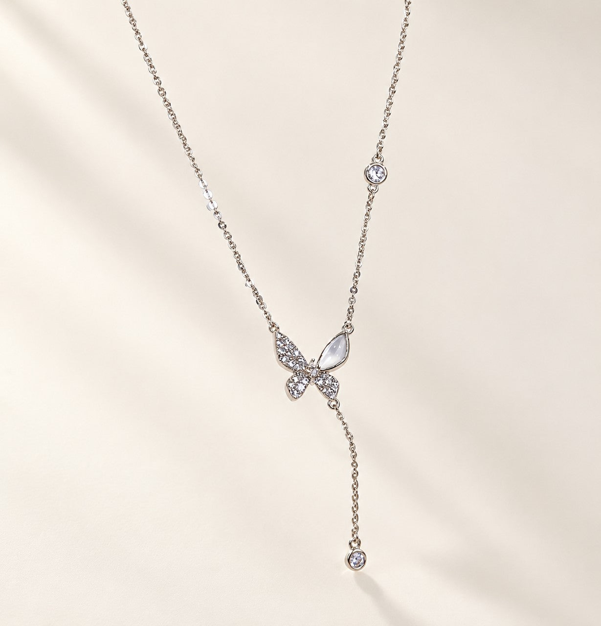 Flatlay view of a silver-tone butterfly Y-necklace with a sparkling cubic zirconia and cat’s eye stone pendant.