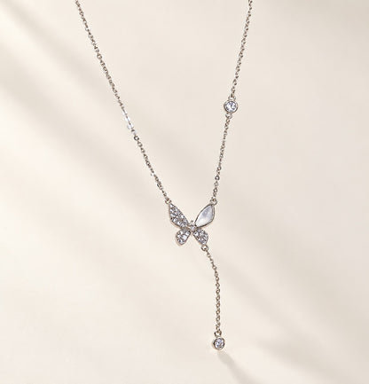 Flatlay view of a silver-tone butterfly Y-necklace with a sparkling cubic zirconia and cat’s eye stone pendant.