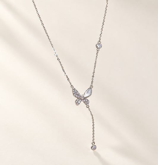 Flatlay view of a silver-tone butterfly Y-necklace with a sparkling cubic zirconia and cat’s eye stone pendant.