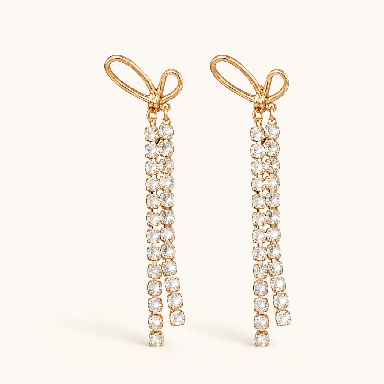 Flatlay view of pair of gold bow dangle earrings with long crystal tassels and 925 silver posts