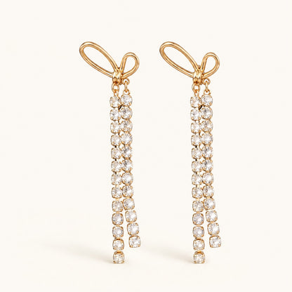 Flatlay view of pair of gold bow dangle earrings with long crystal tassels and 925 silver posts