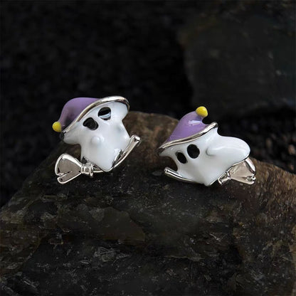 Cute white enamel flying ghost earrings with purple witch hat resting on dark volcanic rock