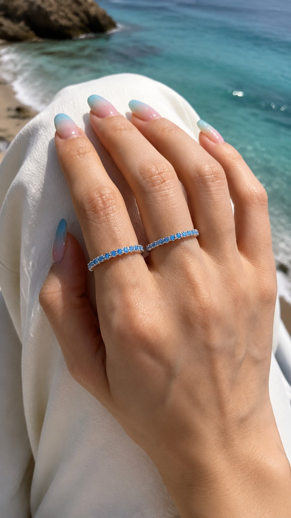 Close-up of model wearing two stacked turquoise eternity open rings against turquoise ocean background