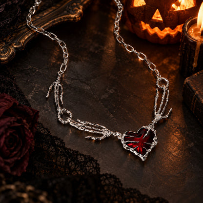 High-angle view of stainless steel gothic red crystal heart choker next to vintage mirror and candles