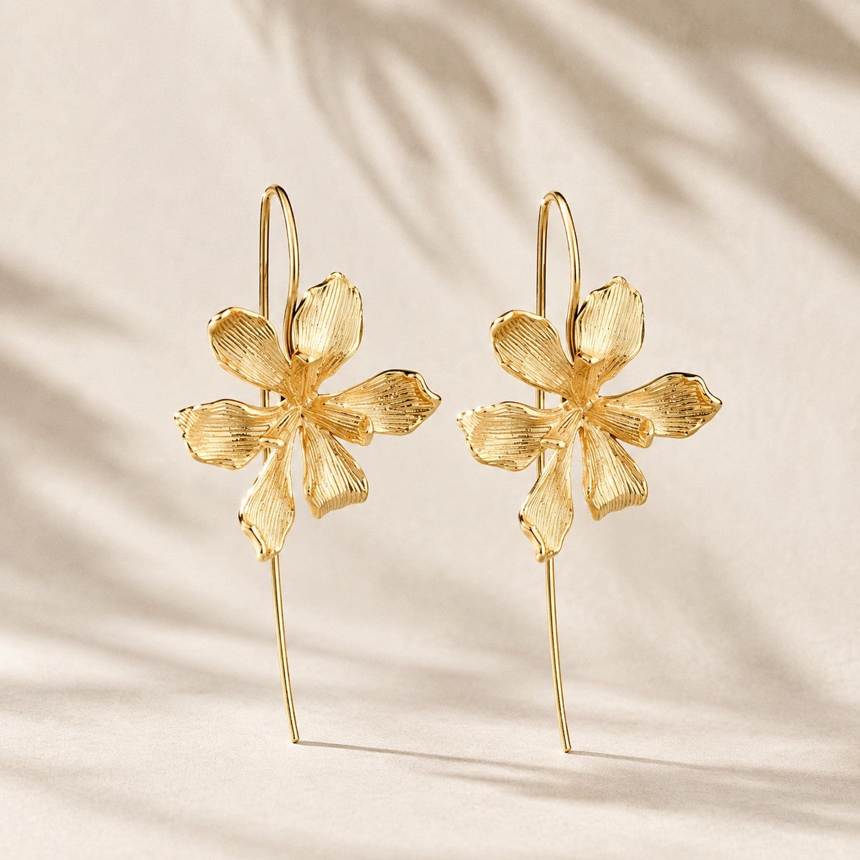 Flatlay view of pair of gold plated textured orchid flower drop earrings with long wire hooks