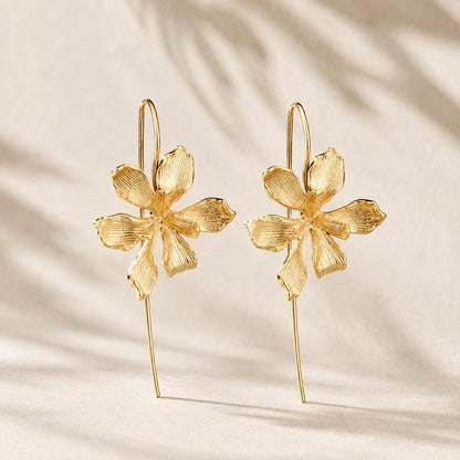 Flatlay view of pair of gold plated textured orchid flower drop earrings with long wire hooks