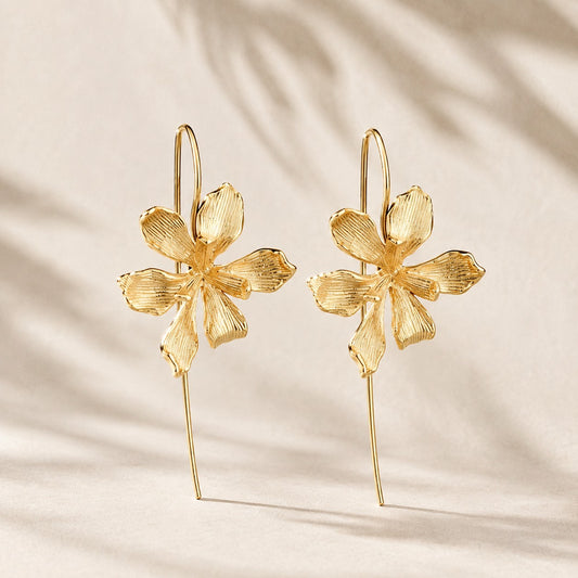 Flatlay view of pair of gold plated textured orchid flower drop earrings with long wire hooks