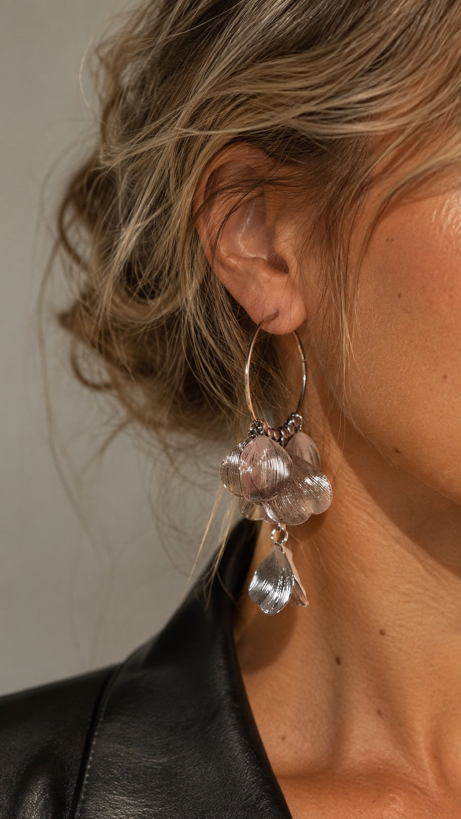 Close-up of a blonde model wearing silver textured petal tassel hoop earrings paired with a black leather jacket.