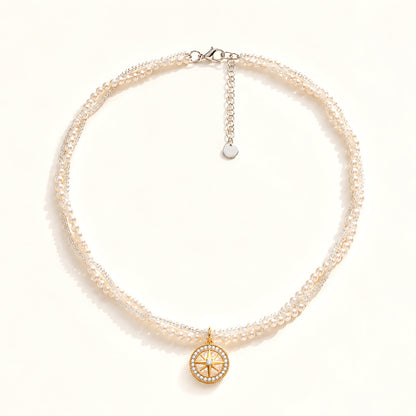 Minimalist flat lay of a double-layer twisted pearl necklace featuring a gold-tone compass and zirconia pendant on a white background.