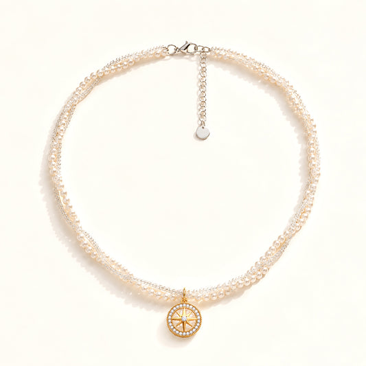 Minimalist flat lay of a double-layer twisted pearl necklace featuring a gold-tone compass and zirconia pendant on a white background.